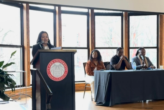 Mary Liz Nogueras speaks at a podium at the Symposium